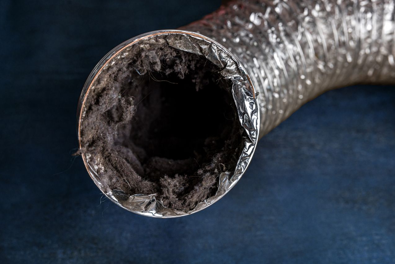 A dirty laundry flexible aluminum dryer vent duct ductwork filled with lint, dust and dirt against a blue background Nettoyage d'une VMC à Bordeaux avec notre contrat d'entretien
