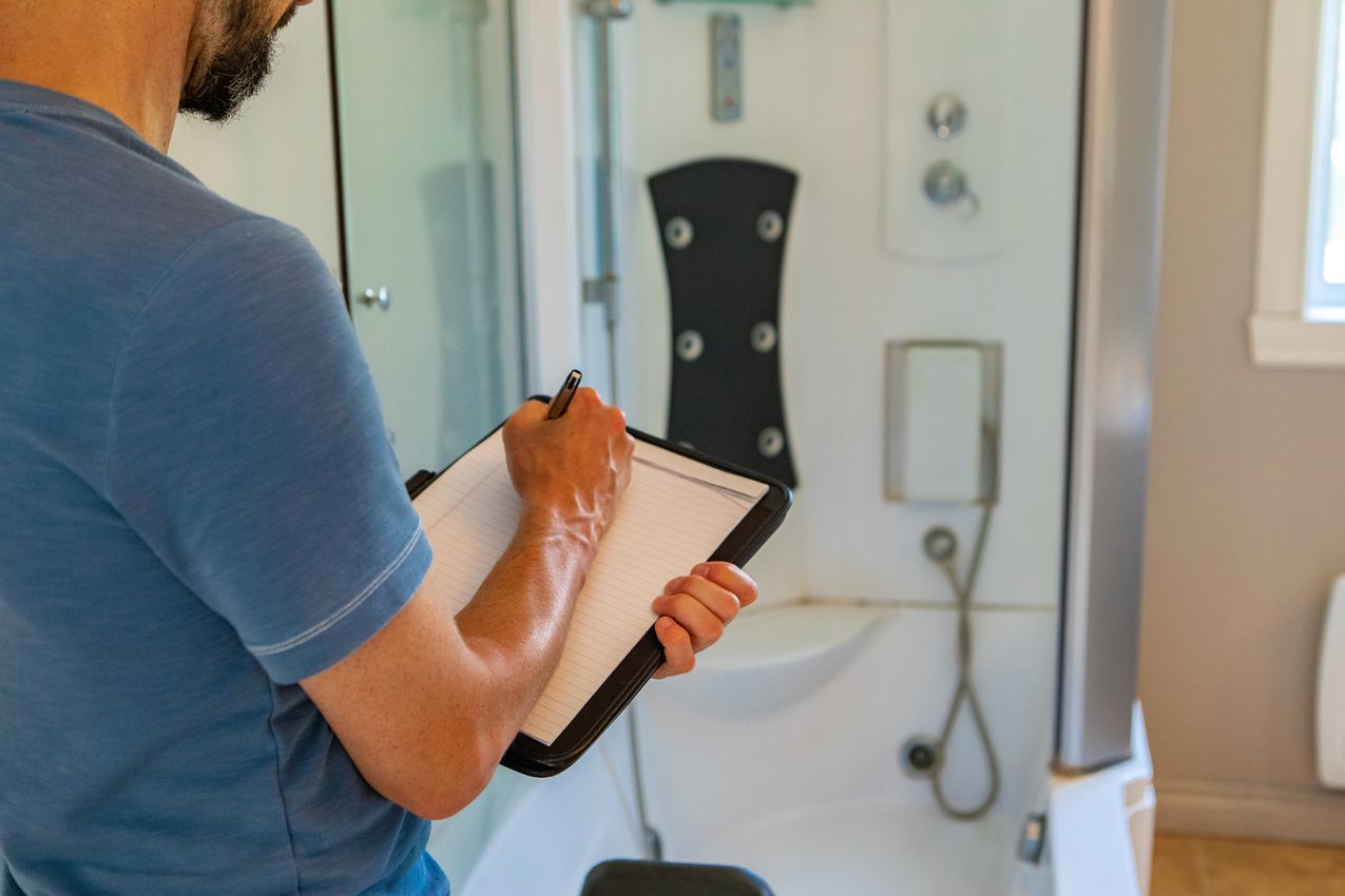 Indoor damp & air quality (IAQ) testing. A close up and rear view of a man using a notepad and pen during a home inspection inside a bathroom, with blurry shower cubicle in background and copy-space. Diagnostic de VMC dans une salle de bain avec moisissure